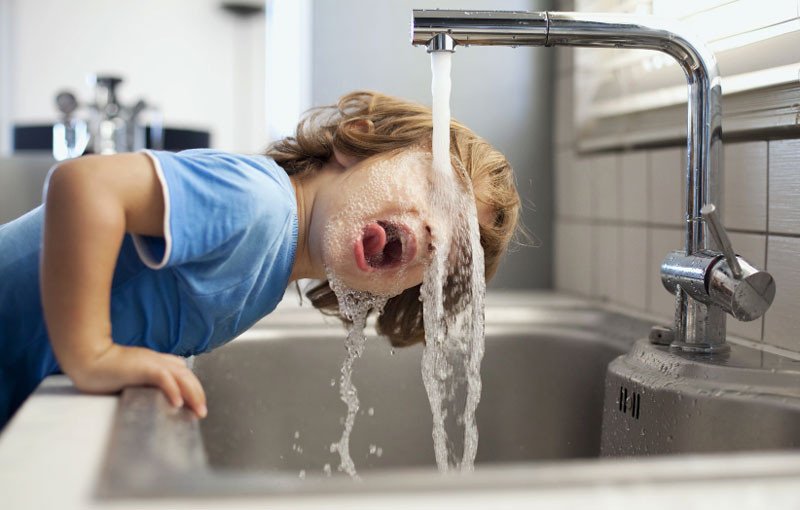 Boy washing face under faucet